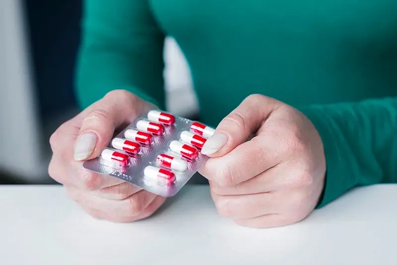 Mãos femininas segurando uma cartela de medicamentos na forma de comprimidos