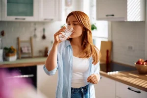 Mulher tomando água, como se estivesse lidando com uma sede que não passa