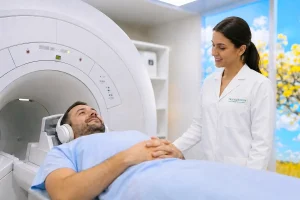 Paciente deitado em uma máquina de ressonância magnética, usando fones de ouvido, enquanto uma profissional de saúde sorridente e de jaleco o assiste.